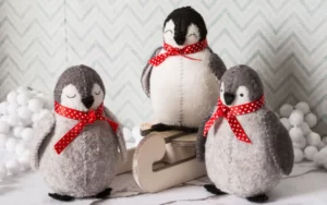 Three handmade felt penguins with red scarves in a snow scene.