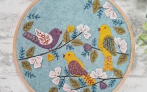 Three beautiful embroidered birds against a pale blue felt background, mounted in an embroidery hoop.